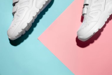 Üst görünüm iki beyaz spor ayakkabı hassas bir geometrik kağıt üzerinde pembe ve mavi arka plan Sert güneş ışığı, metin için boşluk kopyala