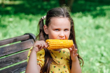 Aile haftasonu parkta güneşli bir günde, çocuk lezzetli mısır yiyor.