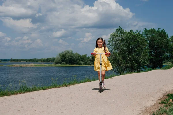 Una ragazza su uno scooter, un weekend in famiglia in un mini viaggio locale, uno scooter per bambini come simbolo di attività familiare e nuova normalità — Foto Stock