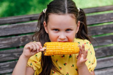 Sarı elbiseli altı yaşındaki çekici bir kızın öğle yemeği için lezzetli bir mısır koçanı var.