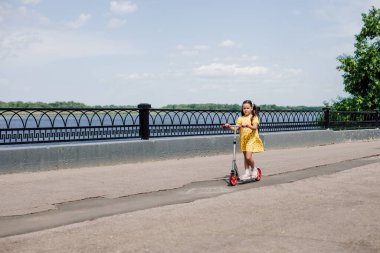 Bir çocuk asfalt bir yolda, nehir kenarında demir bir çitle motosiklete biniyor, bir yaz tatili konsepti olarak motosiklete biniyor.