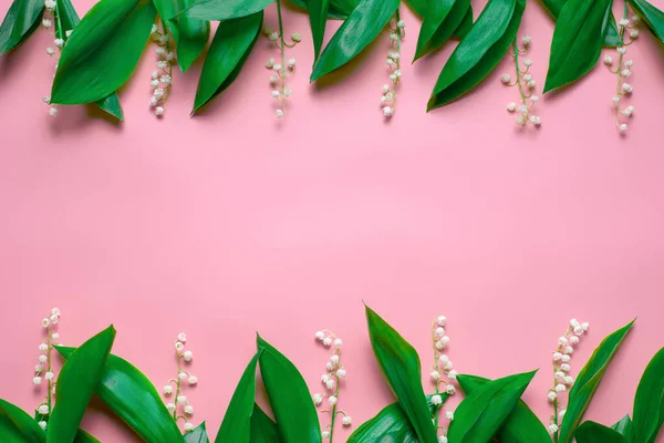 Feuilles vertes et petits bouquets de lys de la vallée comme une bordure florale avec espace de copie. Pose plate avec fond rose — Photo