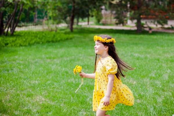 Una chica sonriente en un vestido amarillo y flores amarillas con los ojos cerrados disfruta de un cálido día soleado en el patio trasero de una casa de pueblo — Foto de Stock