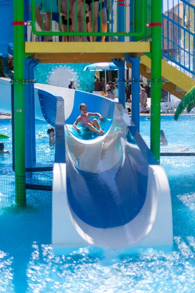 Uma criança em um círculo inflável monta uma corrediça de água em um parque aquático, férias de verão ativas — Fotografia de Stock