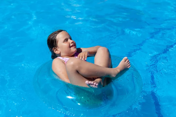 Vidám lány úszó keresztlábú és a szemét becsukva egy kék felfújható kör a szálloda medencéjében egy forró nyári napon — Stock Fotó