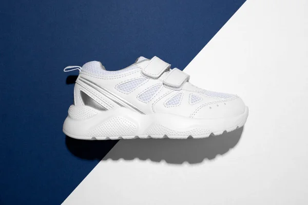 Bovenaanzicht macro op een witte tiener sneaker aan de zijkant met klittenbandsluiting voor eenvoudig schoeisel op een trendy blauw-wit papieren achtergrond met een hard licht — Stockfoto