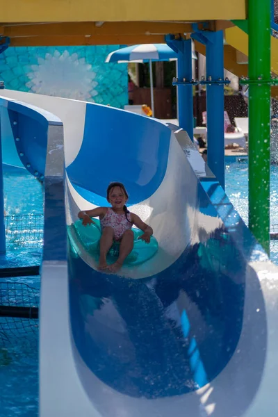 Une fille heureuse pleine longueur dans un maillot de bain rose monte sur un cercle gonflable à partir d'un toboggan dans un parc aquatique par une chaude journée d'été — Photo