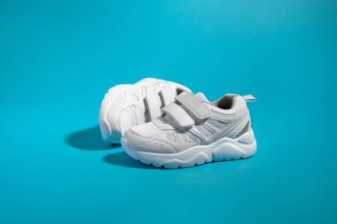 Bir beyaz çocuk ayakkabısı, cırt cırtlı bağcıklar, kolay ayakkabılar, önünde duruyor, mavi kağıt bir arka planda yan yatıyordu.