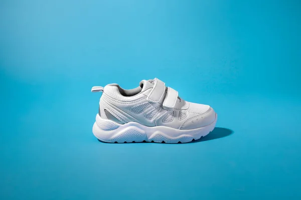 Zijaanzicht van een nieuwe witte kindersneaker met klittenbandsluiting voor comfortabel schoeisel op een geïsoleerde blauwe papieren achtergrond met hard licht — Stockfoto