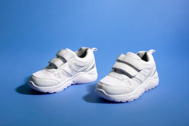 İki beyaz çocuk ayakkabısının yan görünüşü. Cırt cırtlı bağcıklar, arka planda koyu gölgeli mor bir kağıt üzerinde.