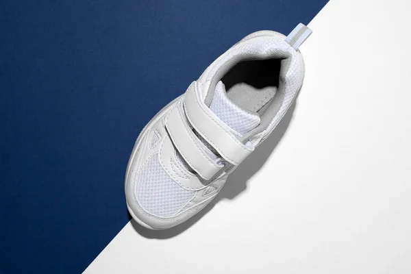 Top view macro σε ένα λευκό παιδικό παπούτσι τρεξίματος με συνδετήρες velcro για γρήγορο shoeing σε ένα μοντέρνο μπλε και άσπρο φόντο χαρτιού με σκληρό φως — Φωτογραφία Αρχείου