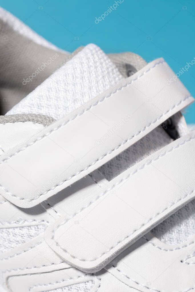 A close-up photo of the Velcro fastener of white sneakers. Childrens sports sneakers made of leather with ventilation made of fabric, sewn with threads on a blue isolated background