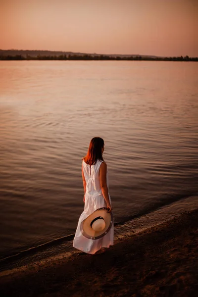 Uma mulher caminha na praia. Visão traseira completa de uma jovem mulher em um vestido branco longo e andar descalço ao longo da costa, relaxando e cuidando da saúde interna e mental — Fotografia de Stock