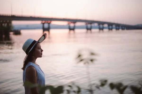 日落时在海边的女人在桥附近的海滩上，一个头戴草帽、头戴草帽、享受夏天和日落的女性形象特写 — 图库照片