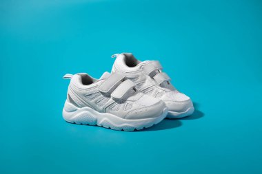 İzole edilmiş mavi bir arka planda sert güneş ışığıyla yan yana duran beyaz spor ayakkabısı reklamı.