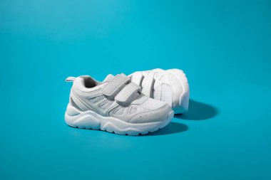 Cırt cırt cırtlı beyaz bir çocuk, sert gölgelerle dolu mavi bir arka planda yan yana yatar.