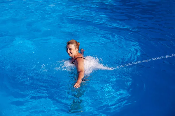 Uma bela mulher caucasiana desfruta de uma hidromassagem nas costas e pescoço com um jato de água em uma piscina exterior de férias — Fotografia de Stock
