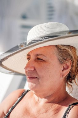 Hasır şapkalı bir kadın. Sahilde gölgede dinlenen beyaz hasır şapkalı çekici bir kadının profil portresi.