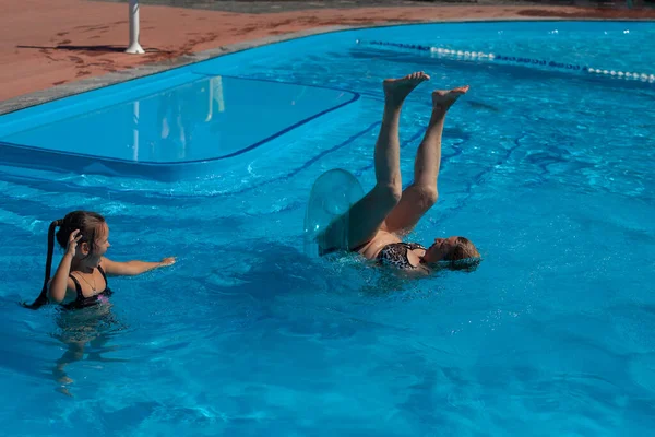 Бабуся і онука в басейні. Бабуся падає догори дном від надувного кола в басейні води, онука сміється і сміється. . — стокове фото