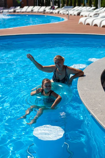 Abuela y nieta en la piscina. Una hermosa abuela y una encantadora chica están sentadas en un bar de la piscina húmeda y alegremente agitando sus manos en un día soleado —  Fotos de Stock