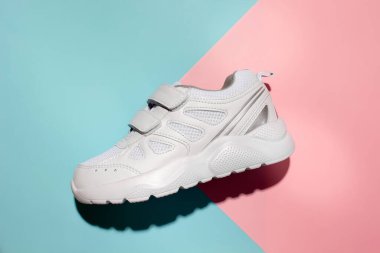 Üst görünüm bir unisex spor ayakkabısı yanında cırt cırt cırtlı bağlayıcılarla hassas bir geometrik kağıt üzerinde sert gölgeli pembe ve mavi arka plan