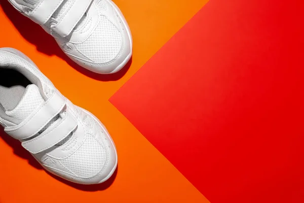 Top view το μπροστινό μέρος των δύο λευκών sneakers με σκληρές σκιές στο πλάι σε ένα γεωμετρικό χαρτί πορτοκαλί και κόκκινο φόντο με αντίγραφο χώρο — Φωτογραφία Αρχείου