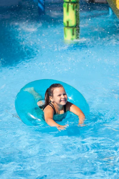 Napfényes nyári nap a vízi parkban. Kis boldog lány úszik tiszta kék víz medence felfújható gumi gyűrű és élvezi a nyaralás a tengeren — Stock Fotó