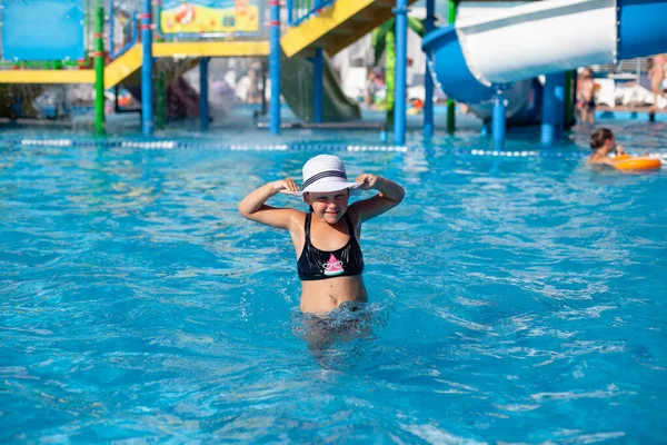 Kind mit weißem Strohhut im Wasserpark. Kleines braungebranntes Mädchen im schwarzen Badeanzug mit Wassermelonenmuster in Sonnenbrille posiert im Pool und genießt den Sommerurlaub — Stockfoto