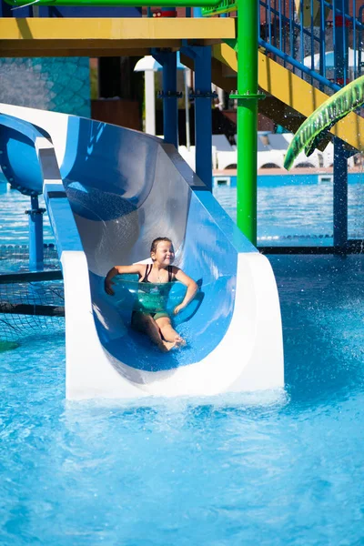 Menina bonito está montando corrediça de água. Criança passa dia ensolarado de verão no parque aquático no resort tropical por mar — Fotografia de Stock