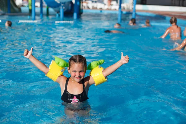 El niño posa en el agua. Feliz niña en flotadores levanta las manos y disfruta de sus vacaciones en el parque acuático —  Fotos de Stock