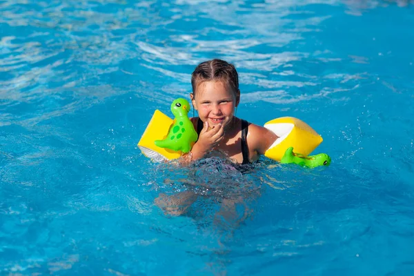 A gyerek úszik a medencében. Boldog kislány úszó dinoszauruszokkal pózol a medencében és megtanul úszni. — Stock Fotó