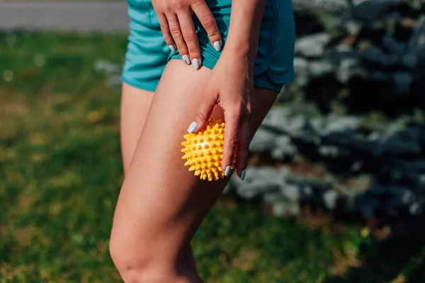 Widok z boku cienki atletyczny ciało młodej kobiety robi masaż biodra z kolczastym piłkę w parku w lecie — Zdjęcie stockowe