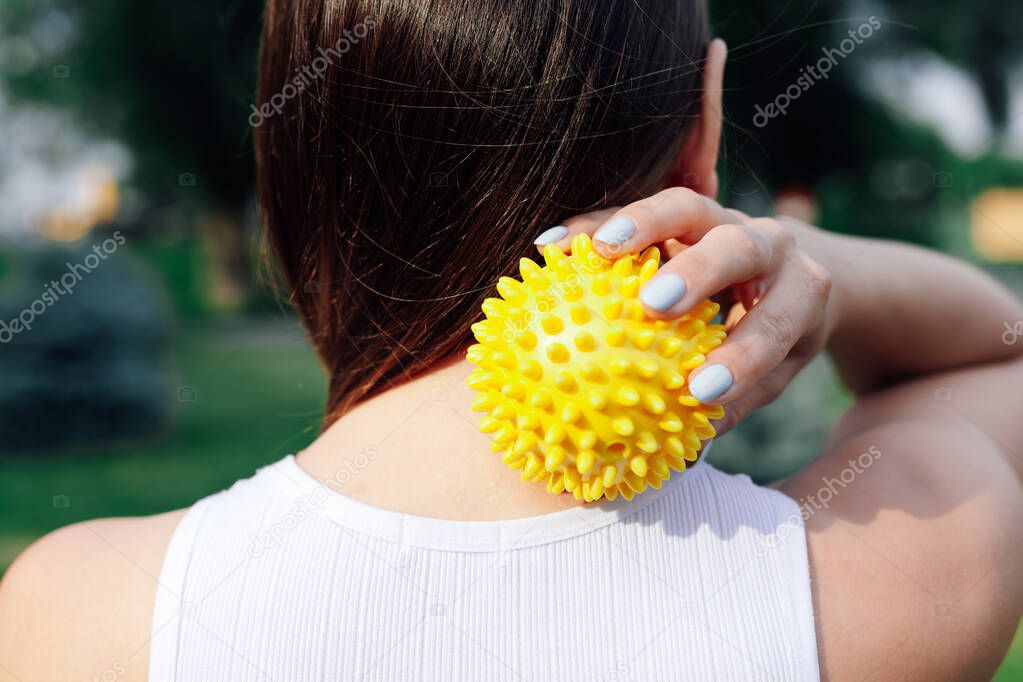 close-up on back of young woman doing neck and shoulder massage with spiky rubber ball, relaxing tense neck muscles