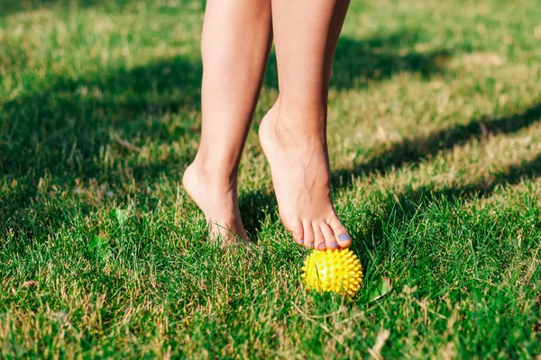 Primo piano di graziosi piedi nudi di giovane donna in piedi in punta di piedi sulla palla da massaggio a spillo sul prato verde dell'estate cortile, concetto di fisioterapia — Foto Stock