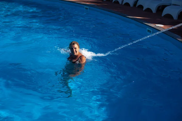 Uma mulher adulta e sorridente desfruta de uma hidromassagem nas costas e pescoço com um jato de água na piscina no spa em uma viagem — Fotografia de Stock