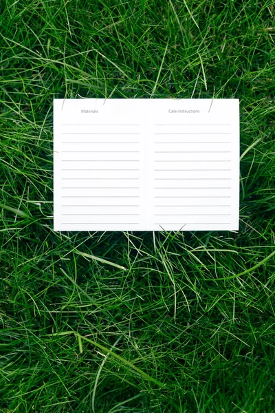 Draufsicht auf einen weißen Karton Blanko-Anweisungen für die Pflege und Materialien Attrappe von Rasen grünem Gras mit Tag für Logo — Stockfoto