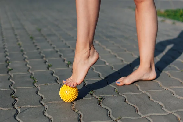 Primo piano di graziosi piedi nudi di giovane donna in piedi in punta di piedi su palla massaggiante a spillo su lastre di pavimentazione all'aperto, concetto di fisioterapia — Foto Stock
