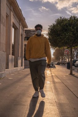 Sarı eşofmanlı Afro-Amerikalı adam arka planda güneşle caddede yürüyor.