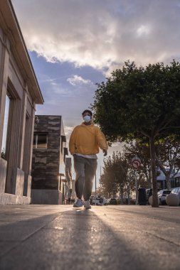 Sarı eşofmanlı Afro-Amerikalı adam arka planda güneşle caddede yürüyor.