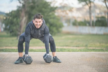 Atletik adam bodur, sırt egzersizi yapıyor ve dambıllarla çapraz antrenman yapıyor.