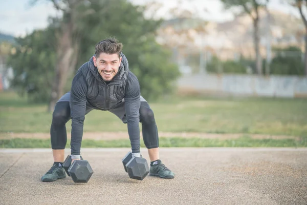 Atletik adam bodur, sırt egzersizi yapıyor ve dambıllarla çapraz antrenman yapıyor.