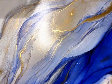 Abstract blue background with gold. Liquid abstraction with beautiful smudges and stains made with alcohol ink and golden paint. Blue fluid texture resembles sea, watercolor or aquarelle.