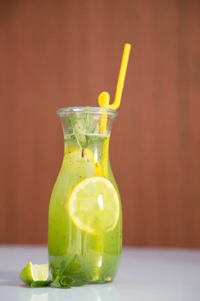 Limonata nella brocca con cannucce e limoni con fondo rosso in legno — Foto Stock