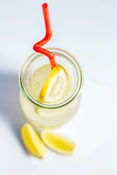 Limonata nella brocca con cannucce e limoni con fondo rosso in legno — Foto Stock