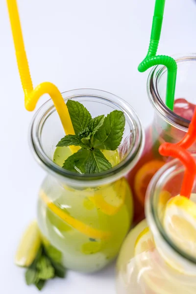 Different tips of lemonade in the jug with straws and lemons on white background — Stock Photo, Image