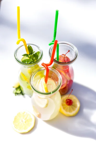 Different tips of lemonade in the jug with straws and lemons on white background — Stock Photo, Image