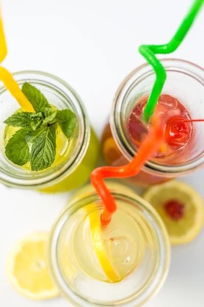 Different tips of lemonade in the jug with straws and lemons on white background — Stock Photo, Image