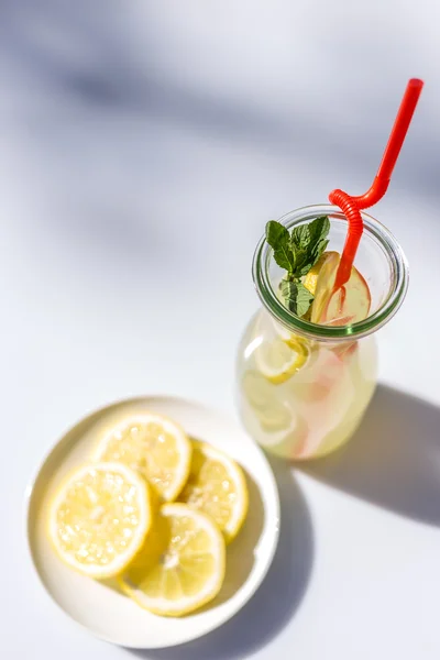 Limonata nella brocca con cannucce e limoni con fondo rosso in legno — Foto Stock