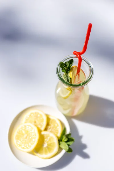 Limonata nella brocca con cannucce e limoni con fondo rosso in legno — Foto Stock