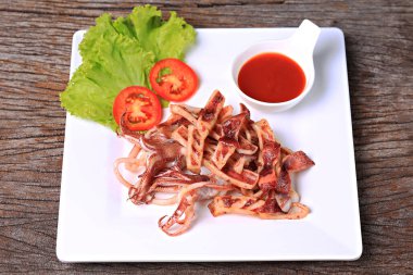 Kızarmış güneşte kavrulmuş kalamar, beyaz bir tabakta, marul ve domatesle garnitür. 